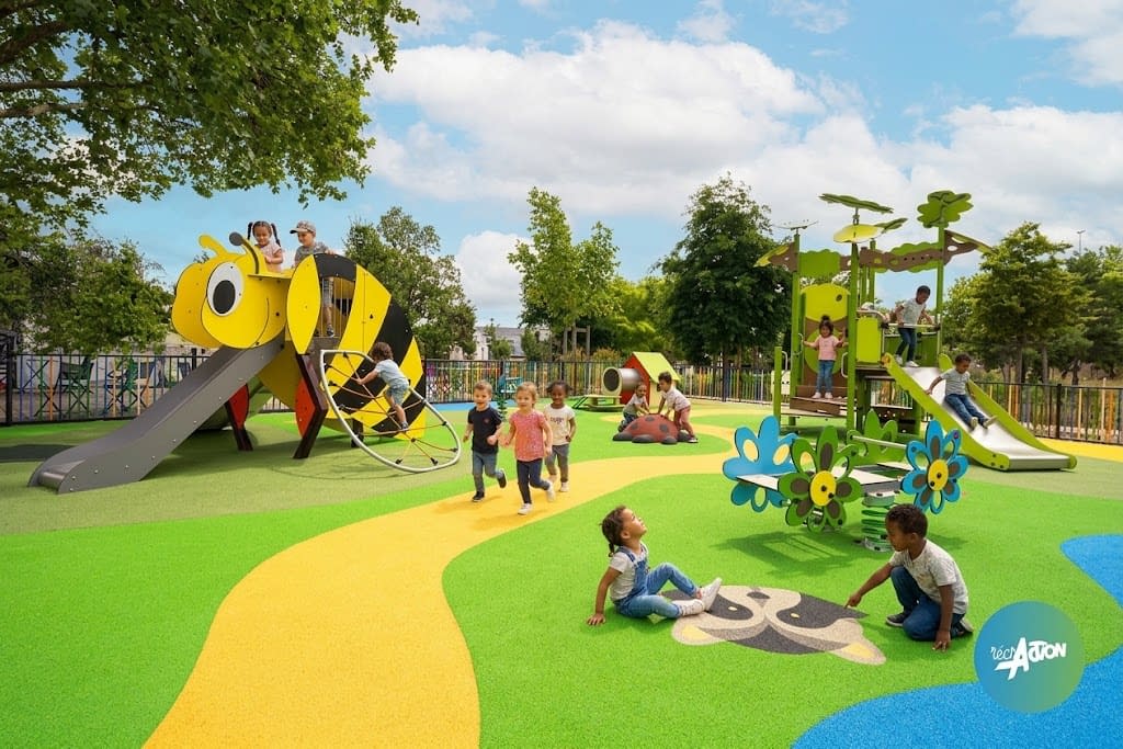 image-aire-jeux-thematique-abeille Aire de jeux thématique en forme d'abeille et de fleurs, enfants en train de jouer sur les jeux et le sol souple coloré