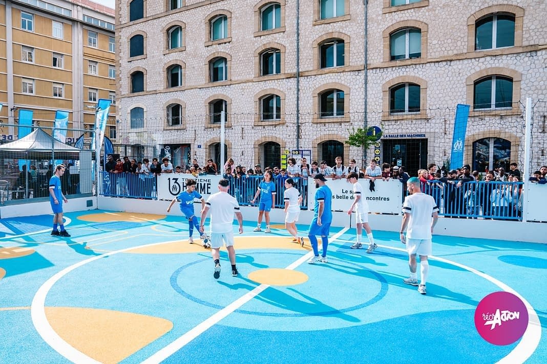 stade-friche-marseille-match Terrain multisport coloré avec des joueurs en plein match, public réuni autour du terrain