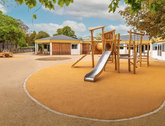 sol-souple-liege-cour-ecole-maternelle Cour d'école maternelle avec un sol souple coulé de teinte liège brun clair délimité par une bordure, autour d'une structure de jeu en bois